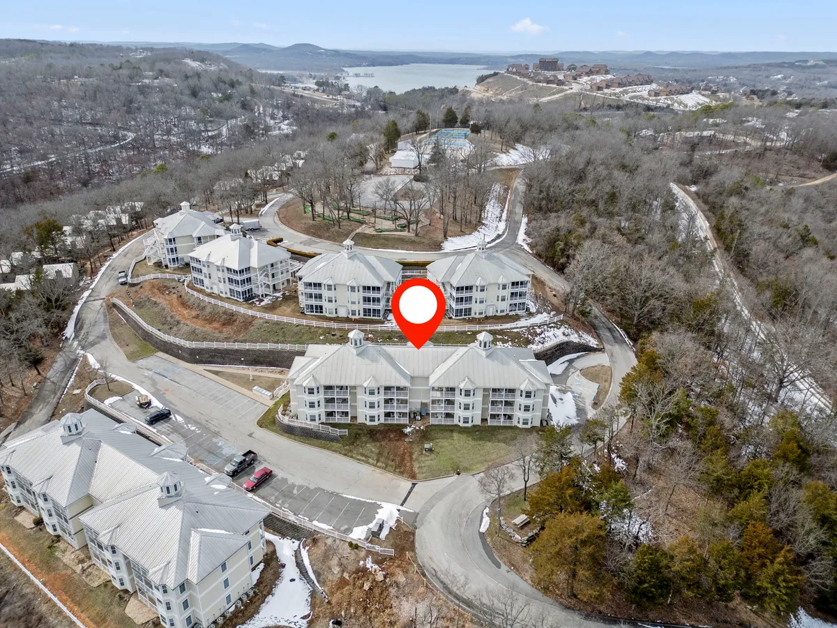 A broad exterior perspective captures the residential buildings surrounded by abundant trees, with a clear view of the lake and gently curving roads. The scene highlights the picturesque setting and the pathways that invite exploration. The peaceful mood and beautiful natural setting suggest opportunities for hiking, watching sunsets, and enjoying year-round outdoor activities.