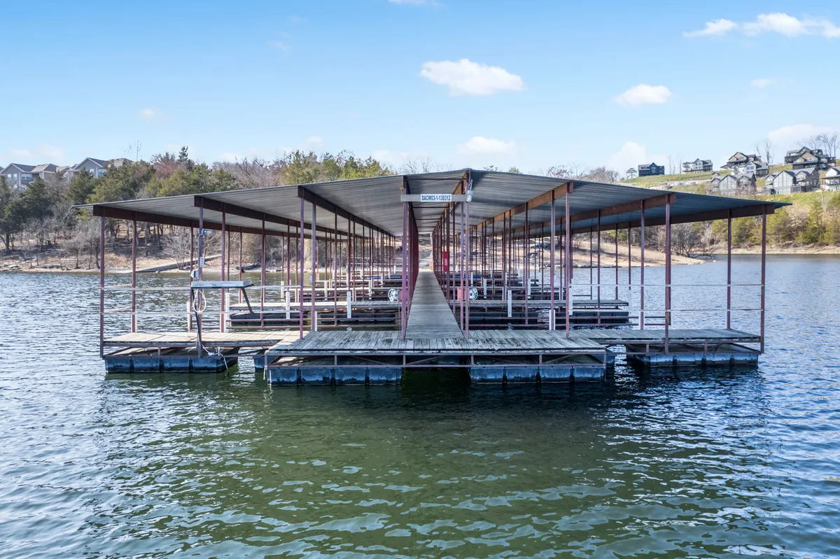A floating dock extends into calm waters, surrounded by natural greenery. The setting suggests a quiet spot for gathering, launching boats, fishing, or simply enjoying the lake's tranquility. The dock is accessible, inviting guests to engage with the water directly.