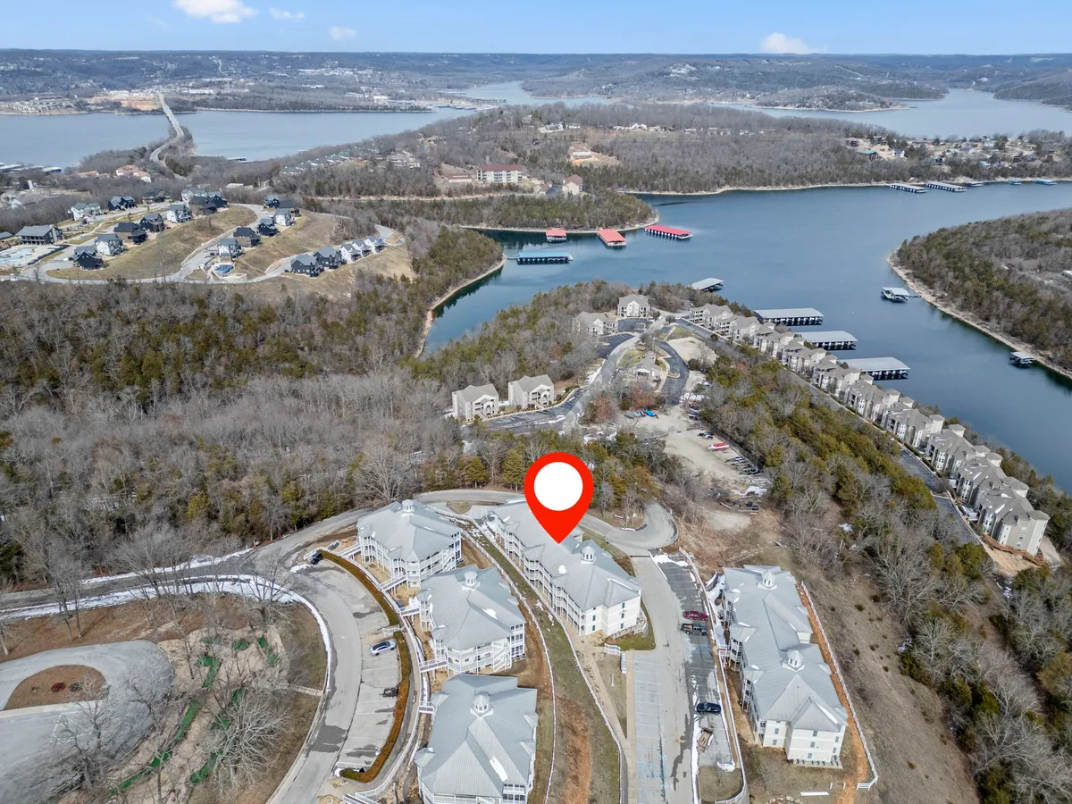 A peaceful exterior shot of the waterfront, surrounding buildings, and lush landscape, suggesting proximity to the lake. The tranquil mood and visible gathering places evoke opportunities for group outings, picnics, or sourcing fresh produce locally before returning to cook in-suite.