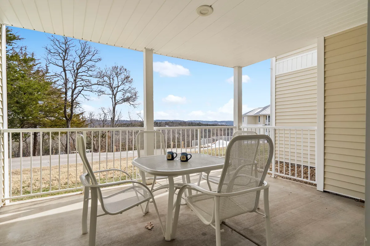 The image features the condo’s outdoor seating area, with a table set for two and coffee mugs, overlooking scenic Ozark hills bathed in the soft light of sunrise. The setting suggests a tranquil environment perfect for enjoying peaceful mornings or relaxing evenings, with panoramic views of the rolling landscape.