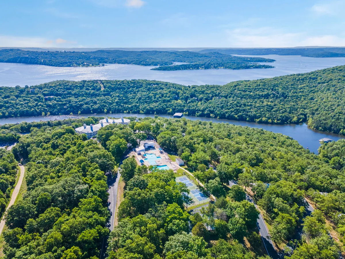 A sweeping view that captures expansive river and hill vistas, a swimming pool area, tennis courts, and lush green surroundings. The scene evokes outdoor recreation, relaxation, and connection with nature.