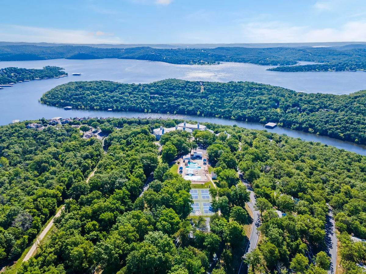 This exterior shot captures a sweeping view of the lake, lush greenery, a sparkling swimming pool, tennis courts, and contemporary resort-style architecture. The setting is tranquil and luxurious, showcasing the variety of outdoor activities available at Ozark Vista 125, from swimming and tennis to boating and hiking along the water’s edge.