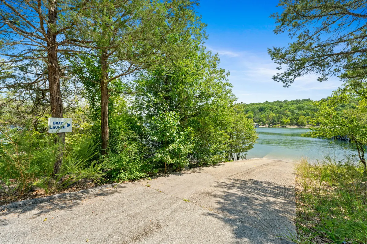 This image showcases a sloped concrete boat ramp leading into the water, surrounded by lush greenery and with clear views of the lake. A prominent 'boat launch' sign is visible, signaling easy access for watercraft. The shoreline is accessible and inviting for both boating and leisure activities.