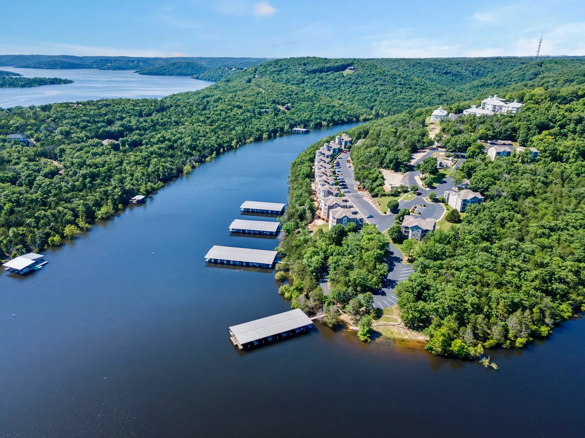 A broad, peaceful view across the lake with residential buildings and docking areas nestled among the greenery. The tranquil water and surrounding trees set a serene, outdoorsy mood, ideal for boating and lake access.