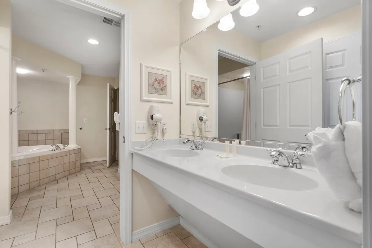 A modern bathroom with dual sinks, a deep soaking tub, and framed artwork. The room feels spa-like, fresh, and serene, ideal for self-care rituals and indulgent bubble baths.