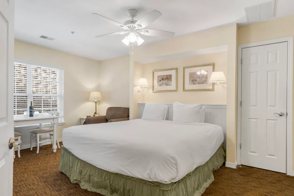 A large, inviting bed sits beneath a window with blinds, accompanied by a soft sofa and tasteful wall art. The space is designed for relaxation and moments of serenity, highlighting a harmonious, restful atmosphere.
