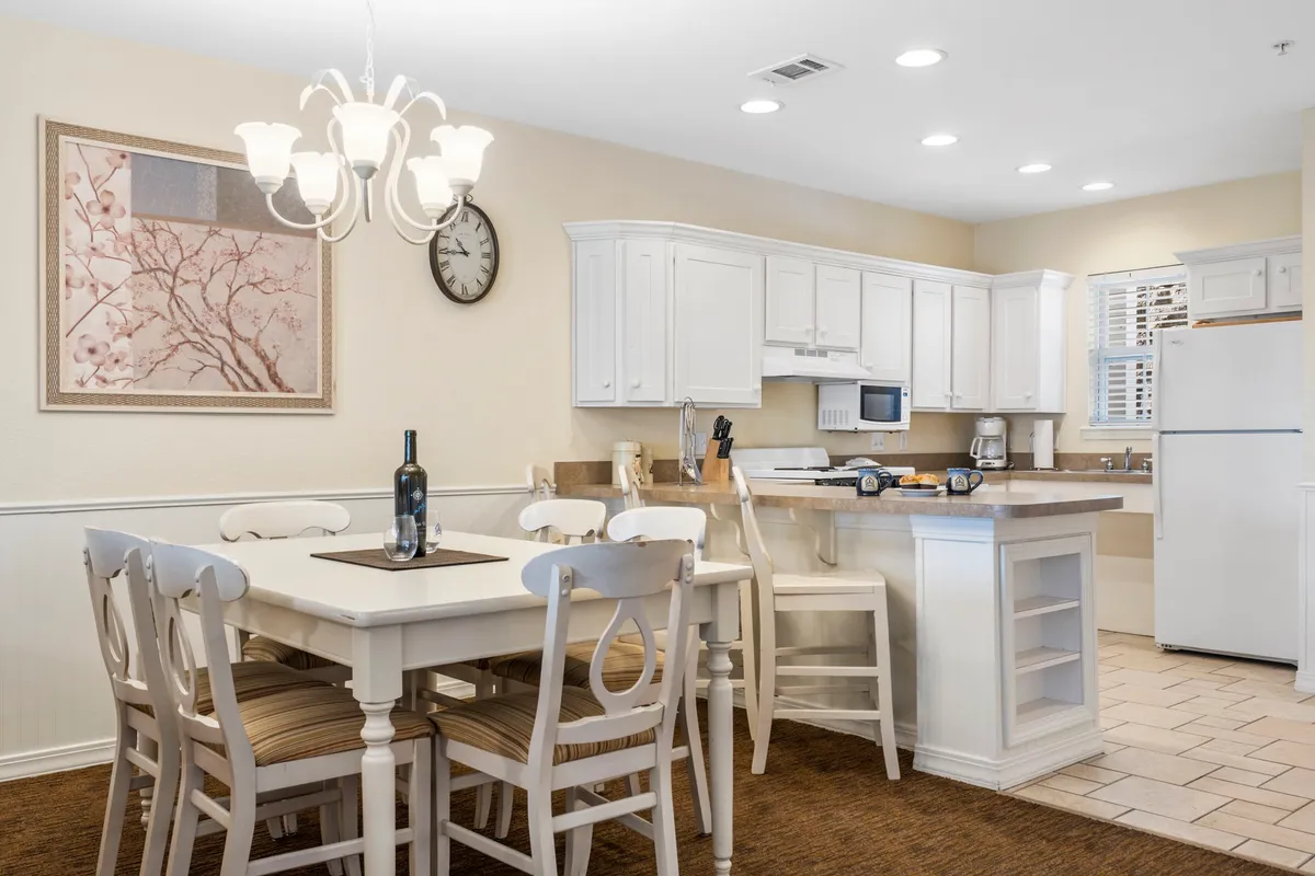 An inviting interior dining space featuring a large table, chandelier, well-appointed kitchen cabinets, and thoughtful wall art. The atmosphere is cozy and perfect for gatherings, family meals, or sharing special moments after preparing food together.