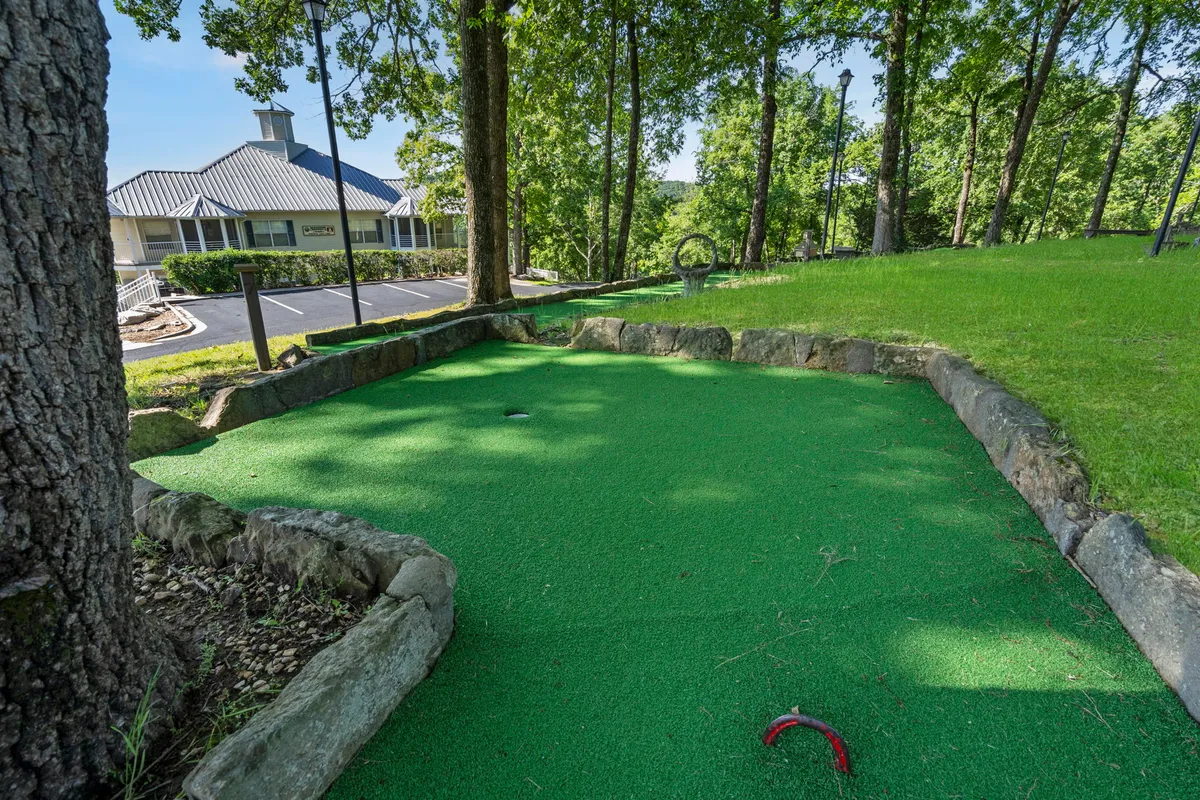 A lively mini-golf area features well-groomed green grass, surrounding trees, and a pathway leading to a building, evoking scenes of groups and families gathering for friendly competitions or casual outdoor games.