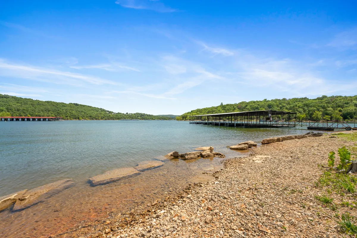 A peaceful view over calm lake waters, with distant green hills in the background, a boathouse visible on the shore, and a rocky natural shoreline. The scene captures the serenity and scenic beauty of Table Rock Lake, ideal for both boating and lakeside relaxation.
