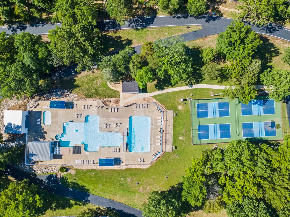 A spacious exterior scene featuring a large swimming pool, tennis courts, and lush greenery. Families and groups can enjoy swimming and tennis amid a relaxing, resort-like setting, highlighting the range of on-site activities available.